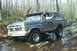 1979 Ford Bronco - A driver navigates a dark gray 1978 Ford Bronco through a rocky, watery trail in a wooded area.