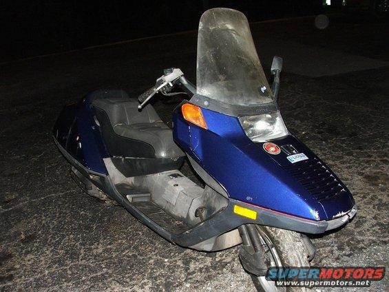 Blue scooter with a tall windshield parked on asphalt