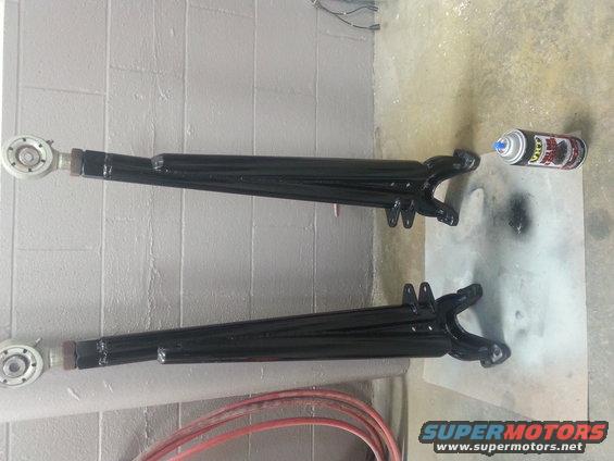 Two black painted control arms with silver ends, next to a can of spray paint