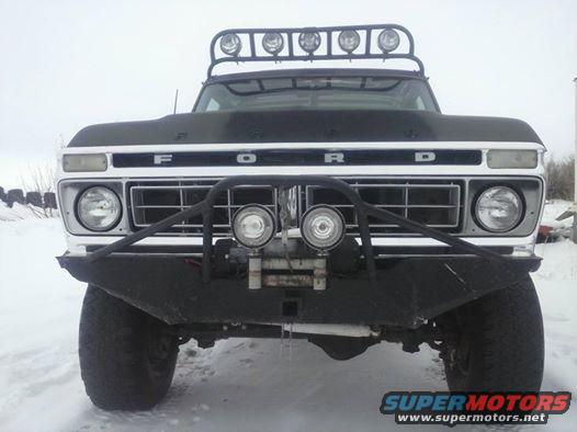 Front view of a black Ford F-Series truck with a winch and light bar, parked in the snow