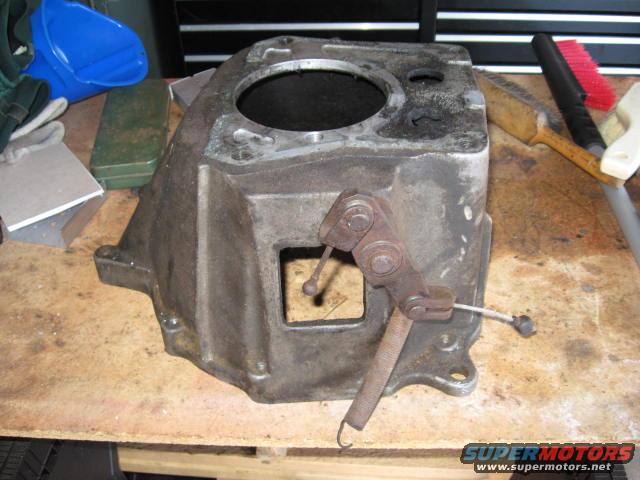 Transmission case with shifter linkage and spring, sitting on a wooden workbench with tools nearby