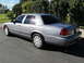 2006 Ford Crown Victoria - A silver sedan is parked on a paved surface with a hedge in the background.