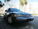 2006 Ford Crown Victoria - A gray 2006 Ford Crown Victoria is shown from a low front angle with palm trees visible behind it.