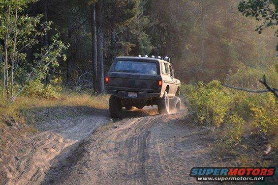 1979 Ford Bronco driving on a dirt trail with trees in the background