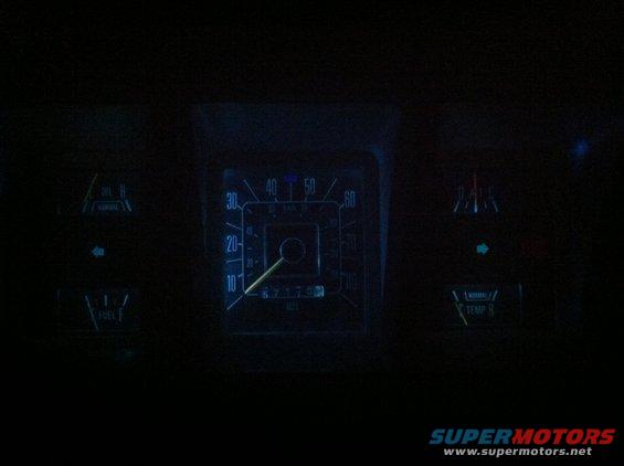 Dark dashboard with illuminated gauges: speedometer, fuel, temperature, and indicator lights