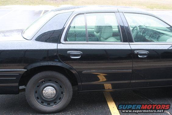Side view of a black sedan with steel wheels parked on wet pavement