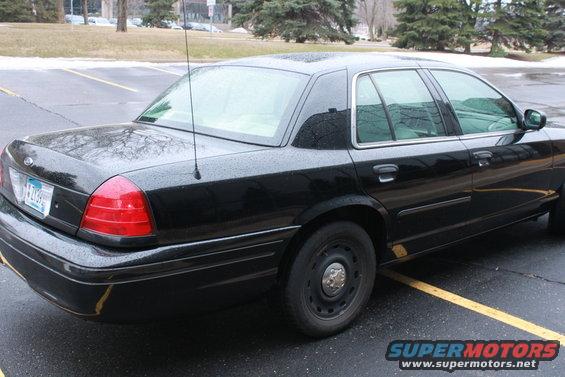Black sedan parked on wet asphalt, rear quarter view. License plate visible