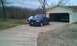 2003 Ford F-150 - A blue 2003 Ford F-150 pickup truck is parked in front of a garage, with another truck visible inside.