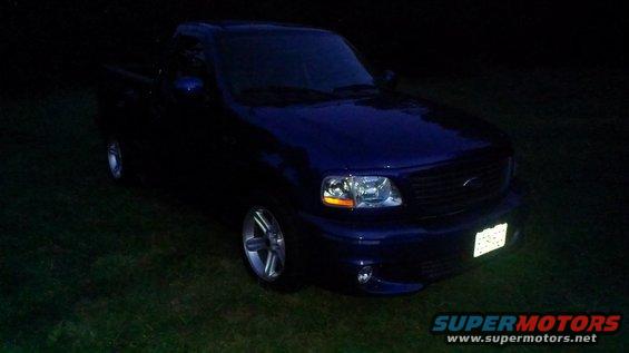Blue 2003 Ford F-150 truck parked on grass at night, front 3/4 view