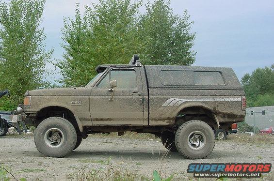 Side view of a 1990 Ford F-150 pickup truck covered in mud, with a camper shell