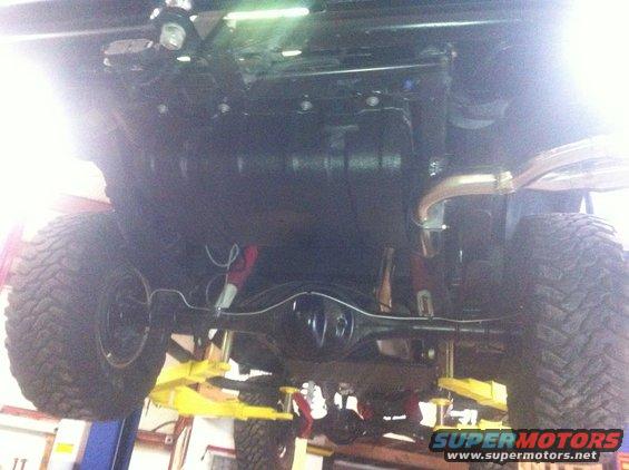 Underside of a vehicle on a lift, showing large tires, suspension, and exhaust