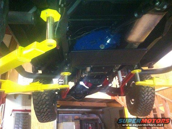 Undercarriage of a vehicle on a yellow lift, showing suspension and drivetrain components