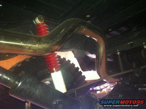 Underside view of a vehicle's exhaust pipe and red shock absorber