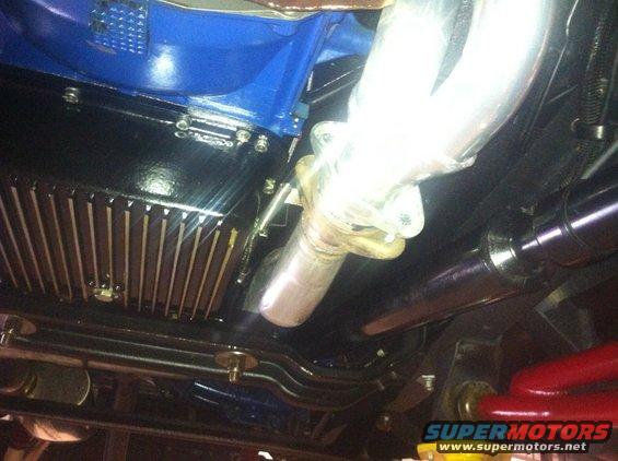 Underside view of a vehicle's engine oil pan, exhaust manifold, and part of the driveshaft