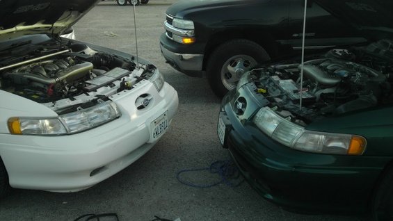 1993 Ford Taurus in white and green, hoods up, parked next to a black pickup truck