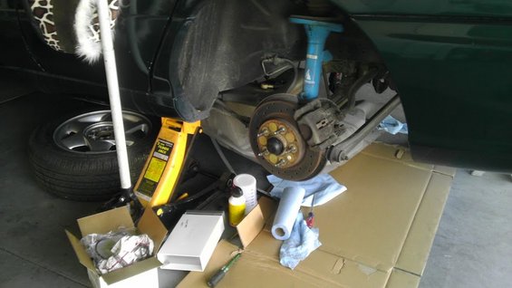 Car's rear brake assembly is exposed with a jack and tools nearby