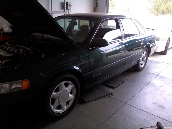 Green 1993 Ford Taurus sedan with hood open, parked next to a white car in a garage