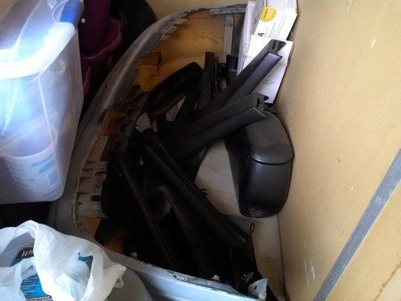 Pile of car parts including a bumper and side mirrors in storage
