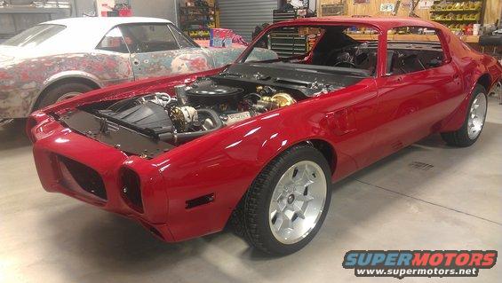 Red Pontiac Firebird with hood open, showing engine bay. Another car in primer is behind it