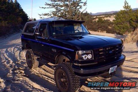 Black 1992 Ford Bronco with blue stripe on sandy terrain