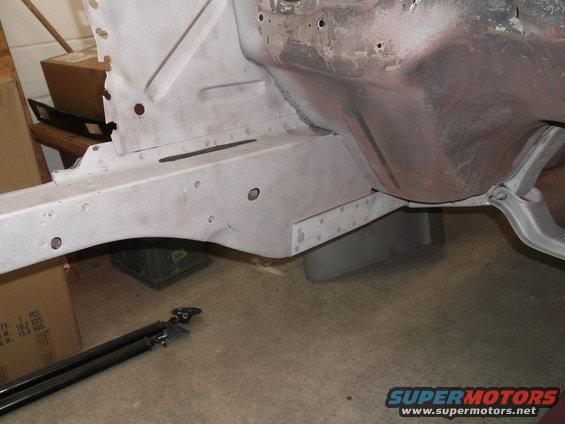 Car frame section, unpainted, with visible rivets and structural supports