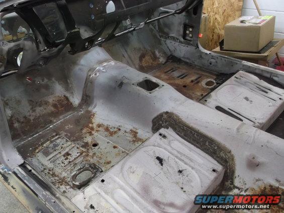 Car interior stripped down, showing rusted floor pans and seat mounts