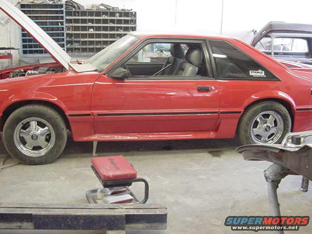 Red coupe with hood open, side view, showing black interior and five-spoke wheels