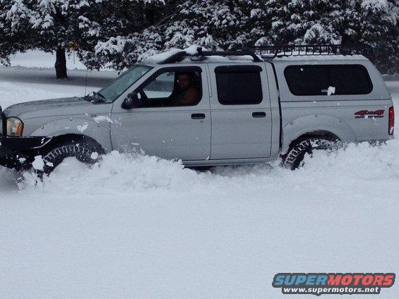 Silver pickup truck with a cap driving through deep snow