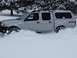 2003 Nissan Frontier - Silver 2003 Nissan Frontier truck driving through deep snow with a cap on the bed.