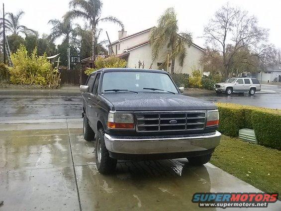 1996 Ford Bronco parked in driveway on a wet day. Another SUV is visible in the background