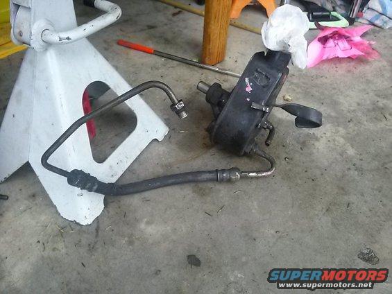 Power steering pump and hoses on concrete floor next to a jack stand