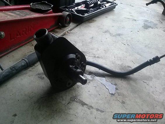 Black power steering pump with hose attached, on concrete floor
