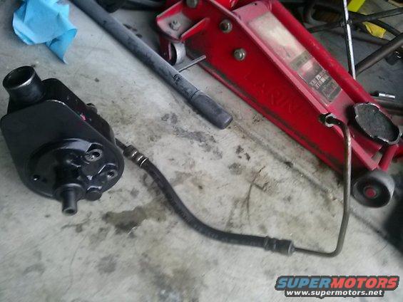 Black power steering pump with attached hose, next to a red hydraulic floor jack