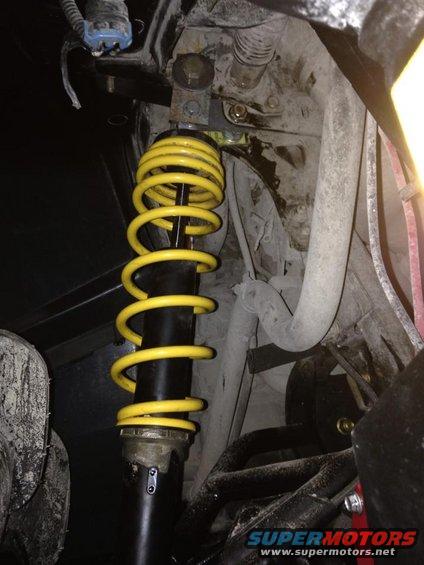 Yellow coilover shock absorber with black body, mounted in vehicle suspension system