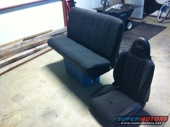 Two black car seats in a garage, one bench seat and one bucket seat