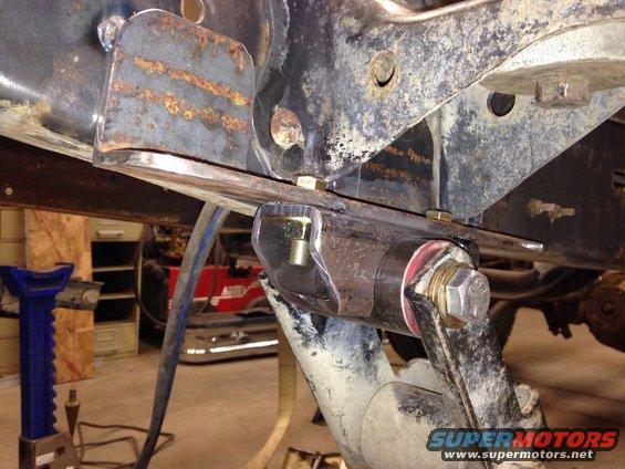 Close-up of rusty vehicle frame with suspension parts and bolts, jack stands visible