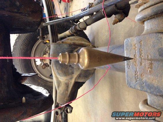 Plumb bob on string measuring alignment of vehicle suspension components. Shows part of a tire and axle
