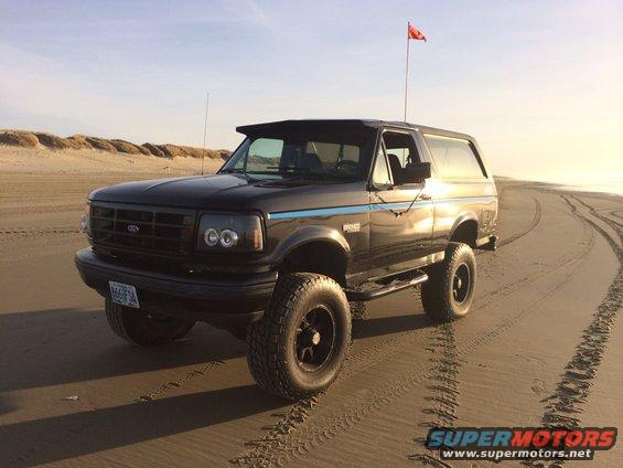 Black Ford Bronco on a sandy beach with a red flag on a pole