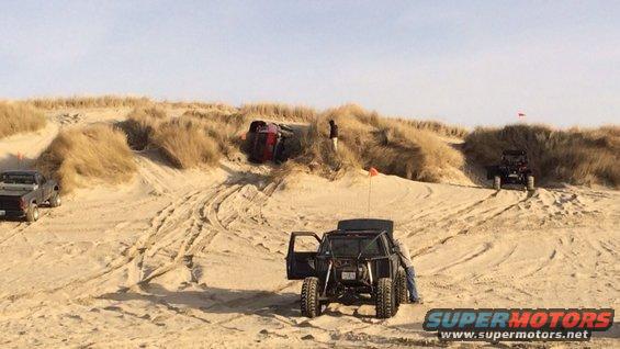 Off-road vehicles on sand dunes, one overturned red vehicle