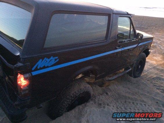 Black Ford Bronco with blue stripe and 'Nite' decal on sand