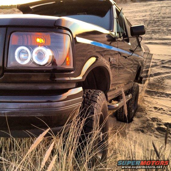 Black Ford Bronco with aftermarket halo headlights, lifted suspension, and off-road tires on a sandy terrain