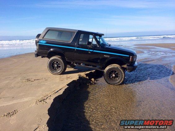 Black 1992 Ford Bronco with blue stripes on beach