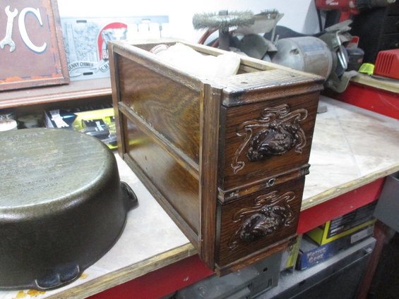 Wooden box with two drawers, ornate carvings, on a workbench next to a cast iron pot