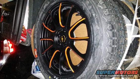 Black aftermarket wheel with orange accents and a winter tire