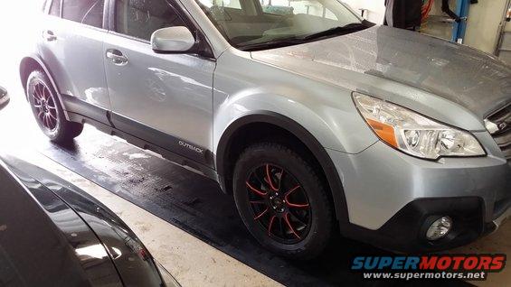 Silver Subaru Outback with black and red rims parked indoors. 'Outback' is visible on the lower door trim