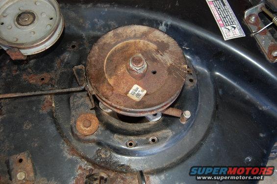 Close-up of a rusty lawn mower deck with a pulley and spring mechanism