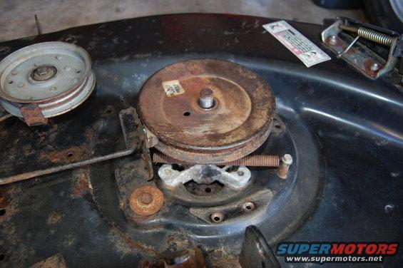Close-up of two pulleys and a spring on a rusty lawn mower deck