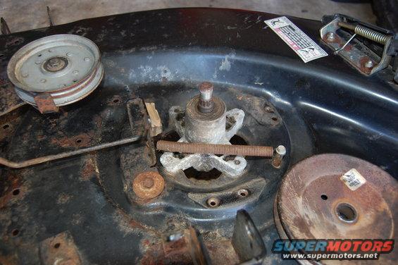 Close-up of a rusty lawn mower deck spindle assembly with pulleys and a spring