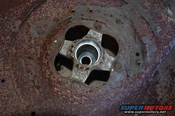 Close-up of a rusted mower deck spindle housing with a four-bolt mounting pattern