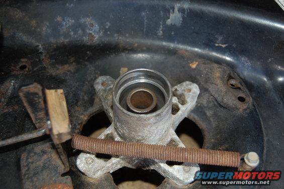 Close-up of a mower deck spindle housing with a rusty spring and metal bracket